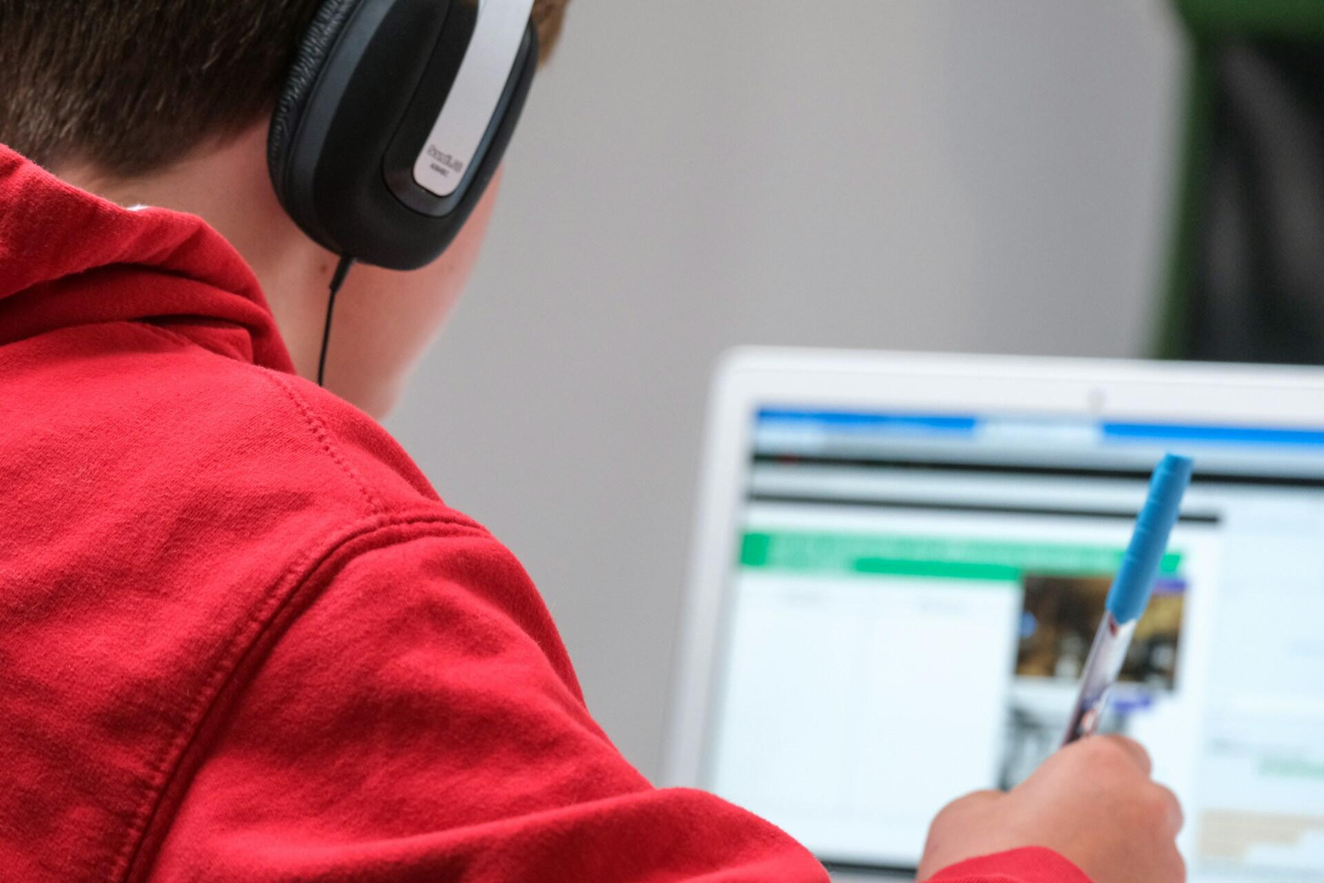 Student wearing headphones and writing notes while using a laptop