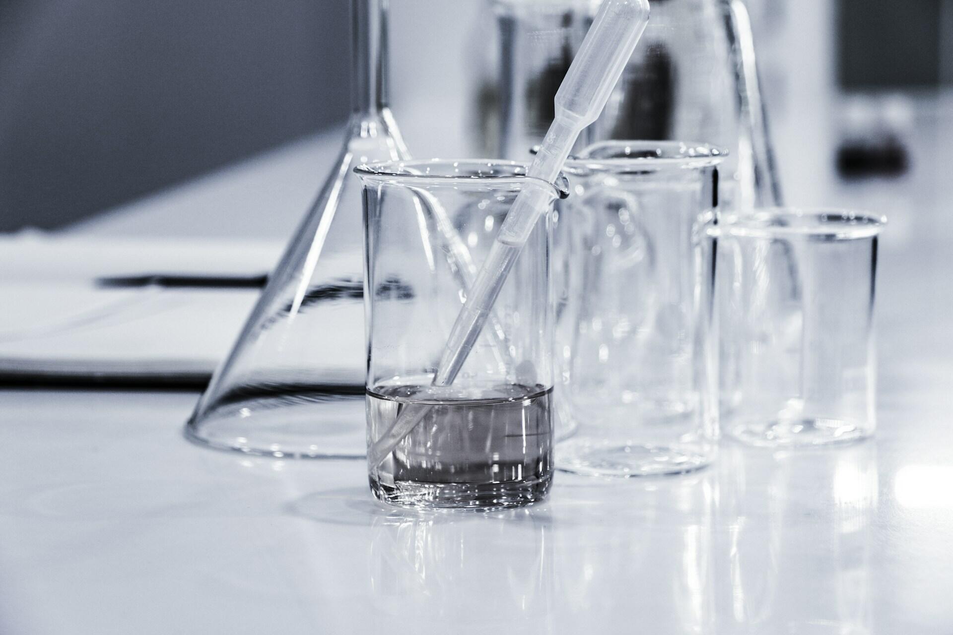 Clear laboratory beakers, flask and plastic pipette on a work surface
