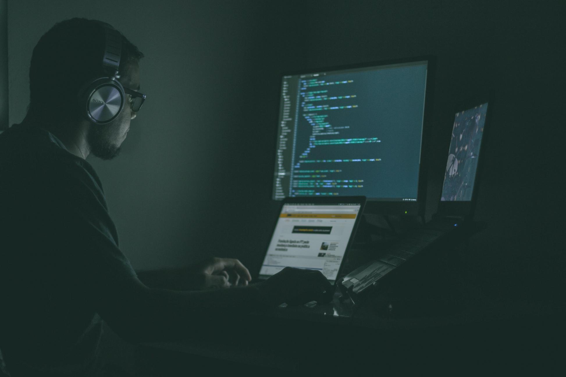 A man in front of the computer working with headphones on.