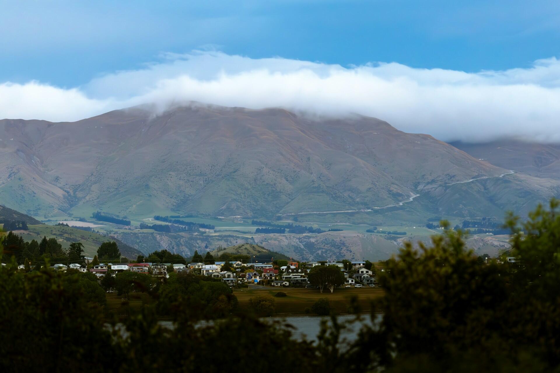 A view of Queenstown, New Zealand, with a long white cloud over it.