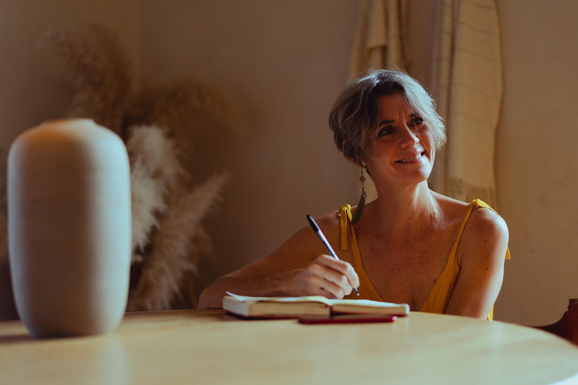 A woman smiles as she writes in a notebook.