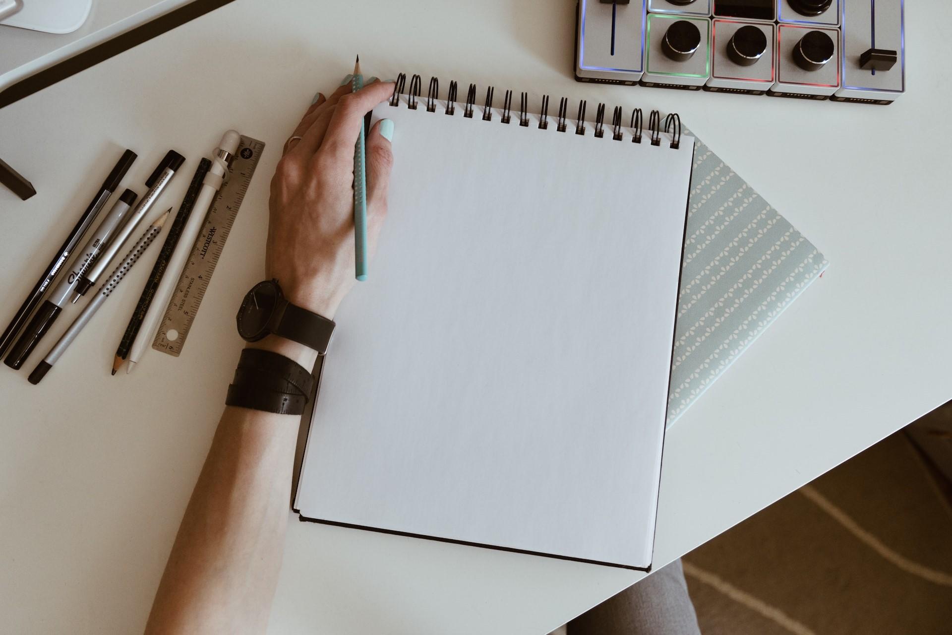 A hand next to a sketchbook with a pencil.