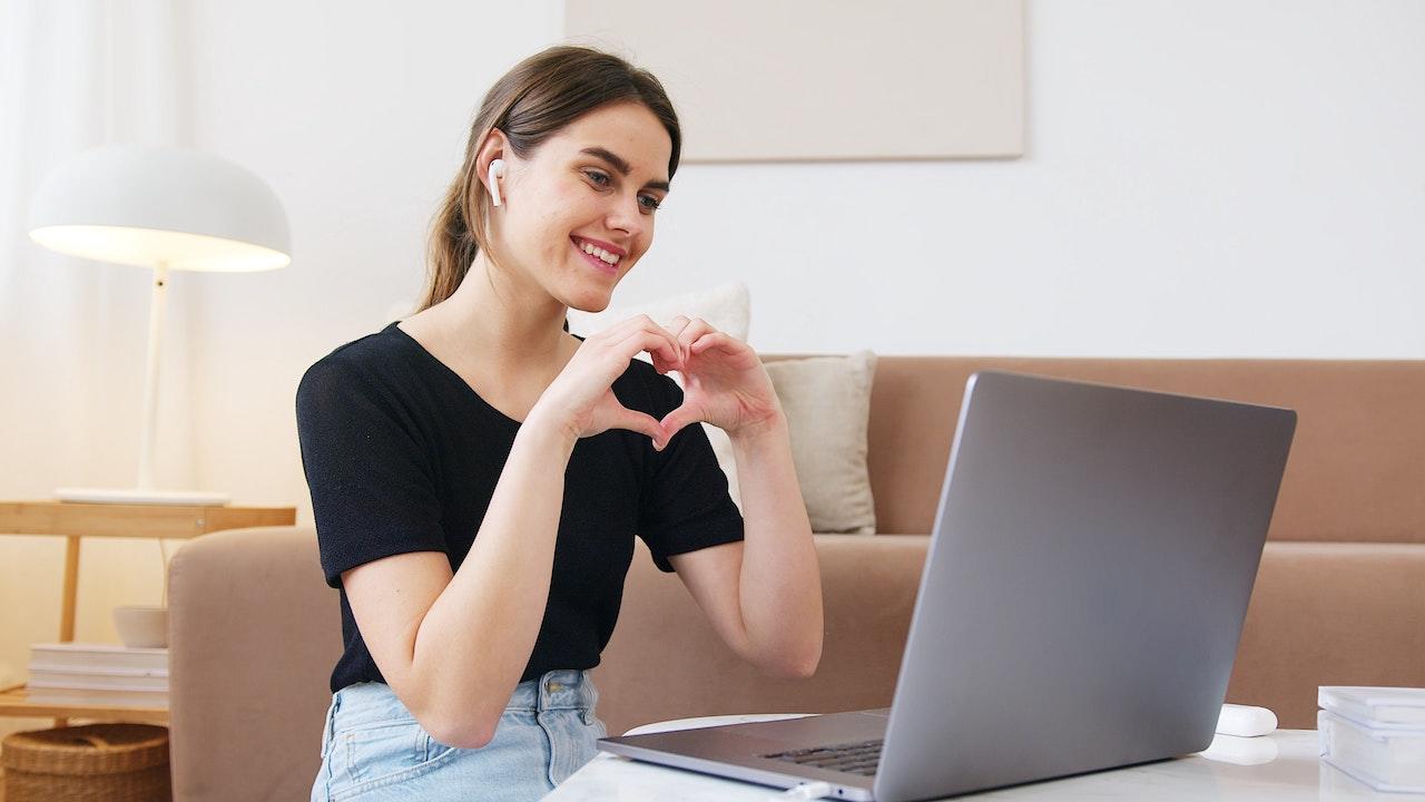A virtual teacher makes a heart hand gesture to their student online.