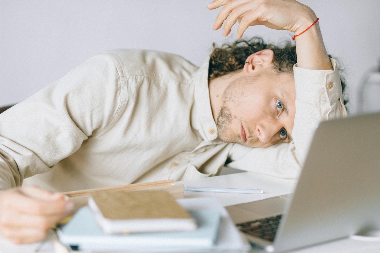 A student looks forlorn as they stare at their computer screen and rest their head on their arm.
