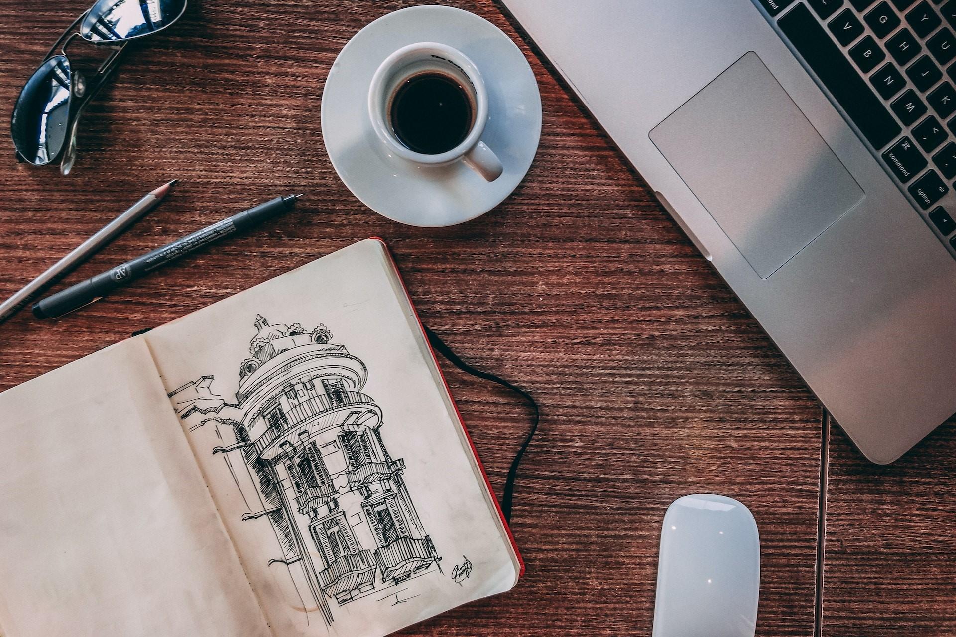 A sketch of a building by a cup of coffee and a laptop.