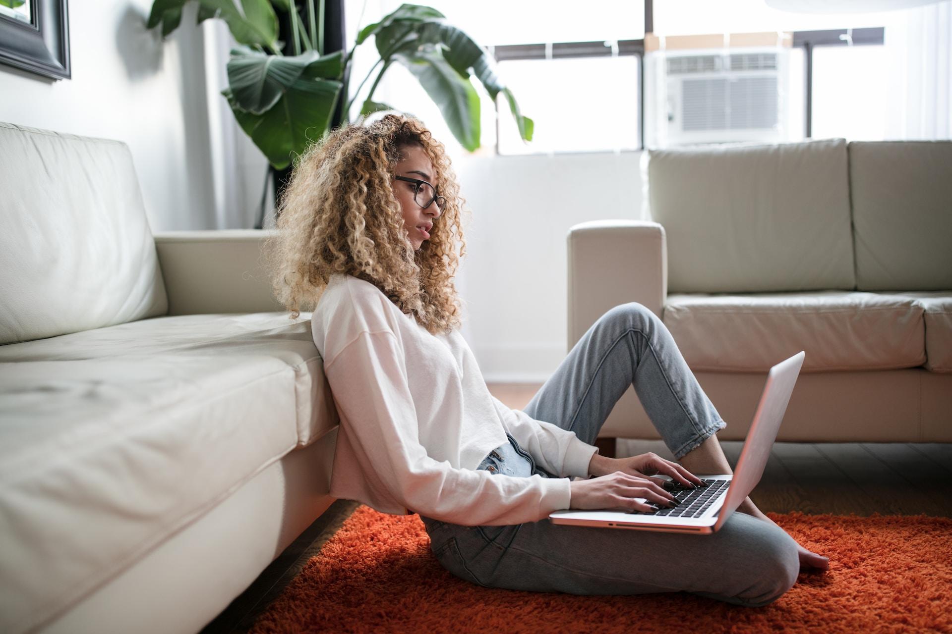 A student on their laptop while sitting on the floor at home