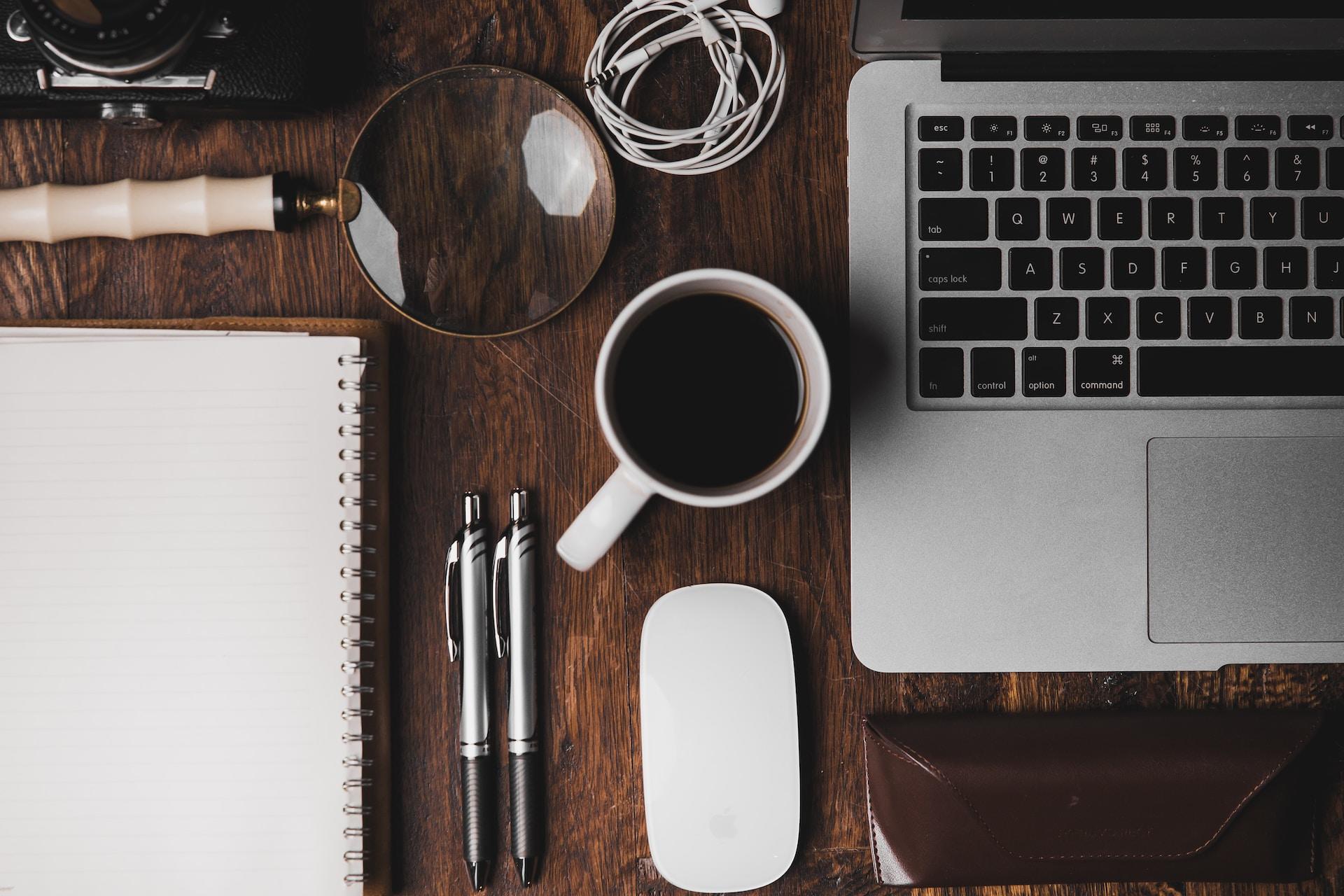 A view of a coffee cup, laptop, mouse, notepad, and stationery.