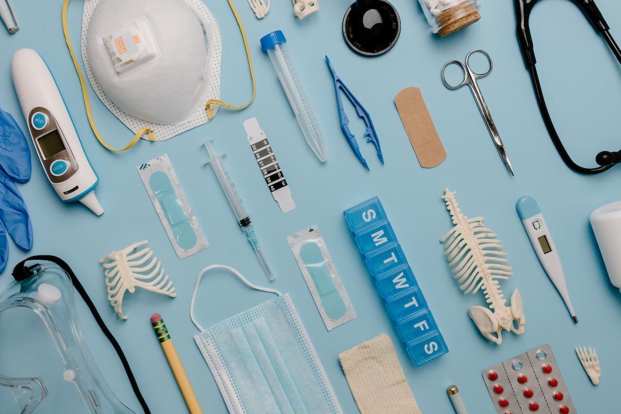 A flatlay of common medial supplies like a syringe, medical mask, pill-planner, and tweezers