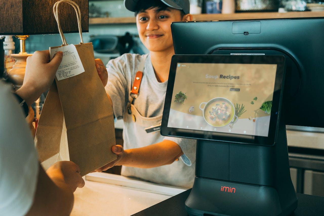 A teen employee hands a bag to a customer.