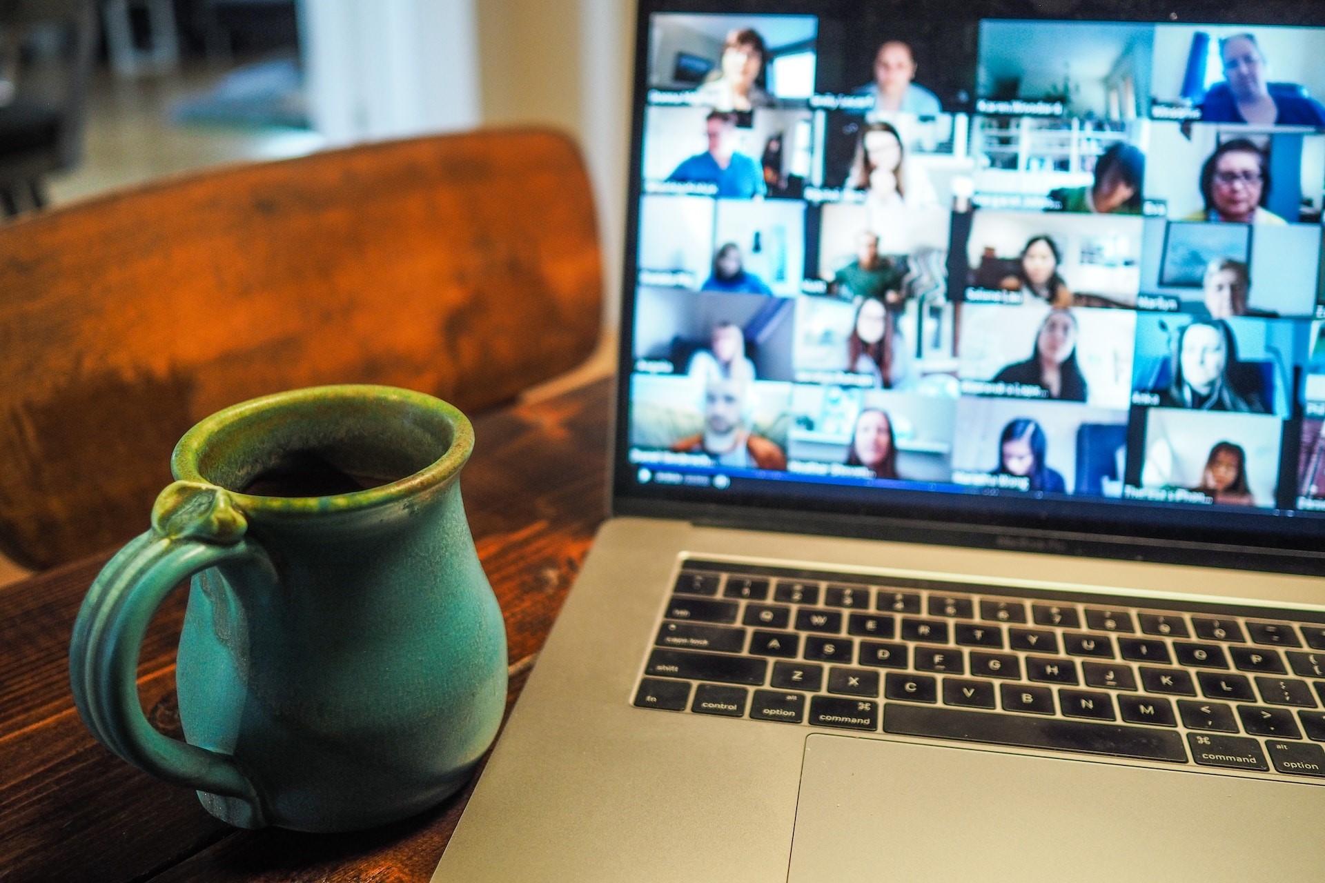 A zoom meeting on a laptop next to a cup.