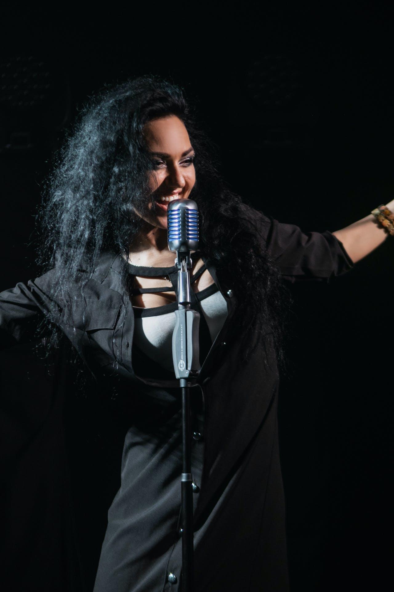 A woman singing into a stand up microphone with stage lights behind her