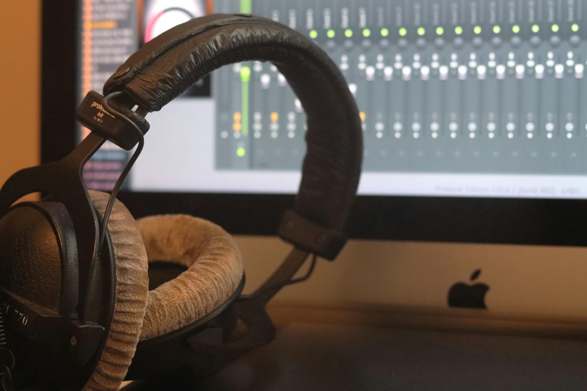A pair of headphones by a Mac running audio recording software.