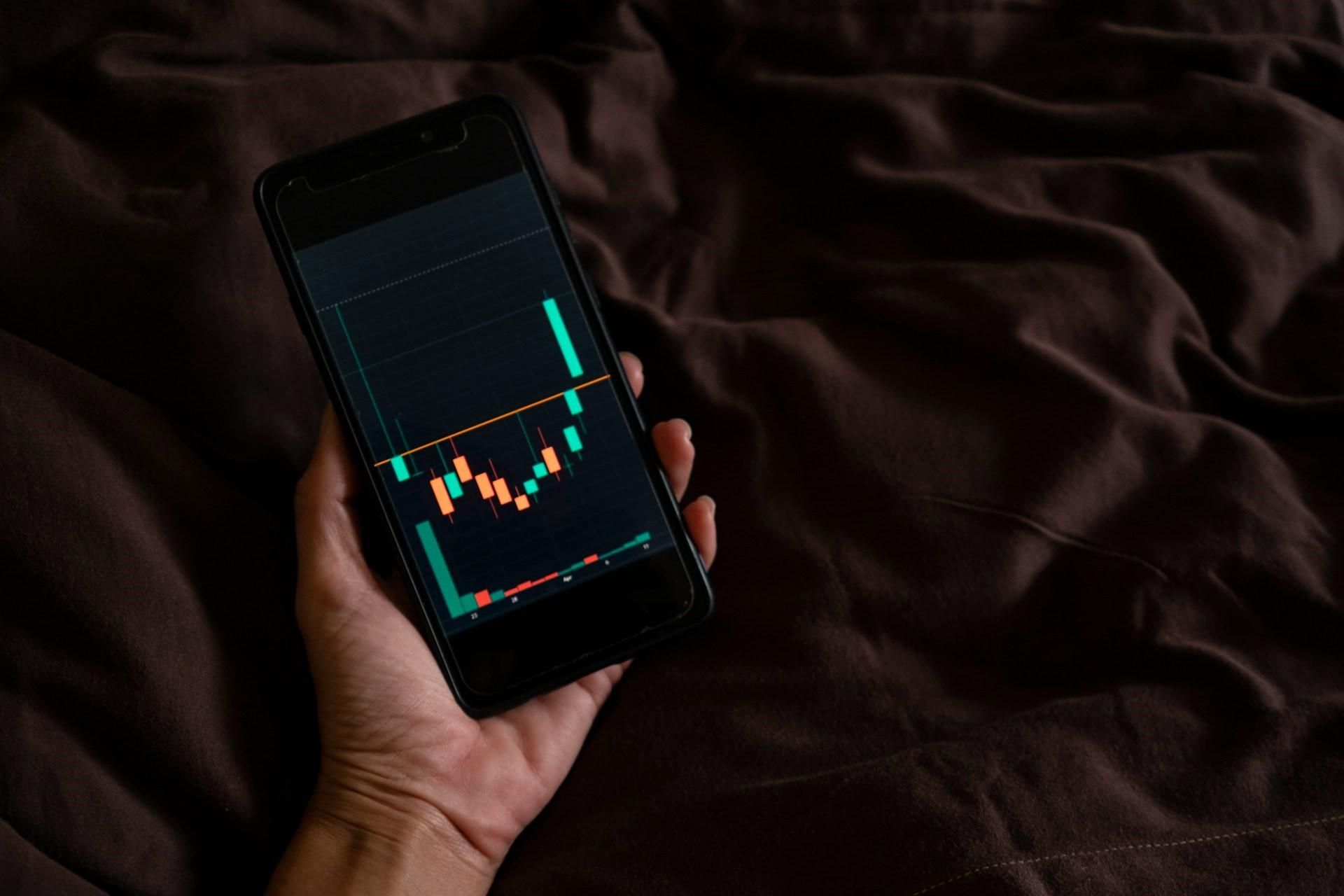 A hand holding a phone with a graph of stocks on it.