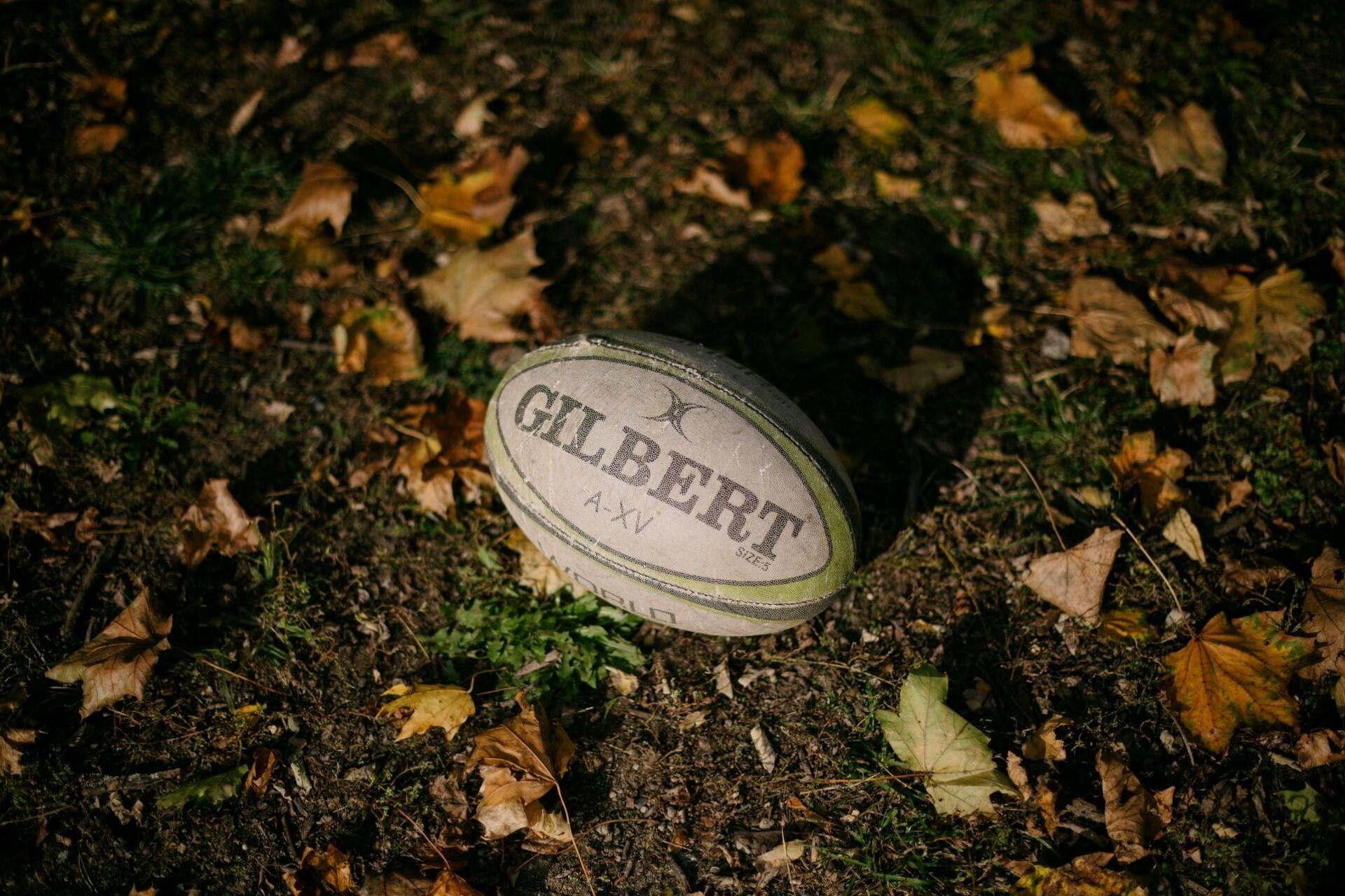 Gilbert rugby ball resting on grass with autumn leaves around it