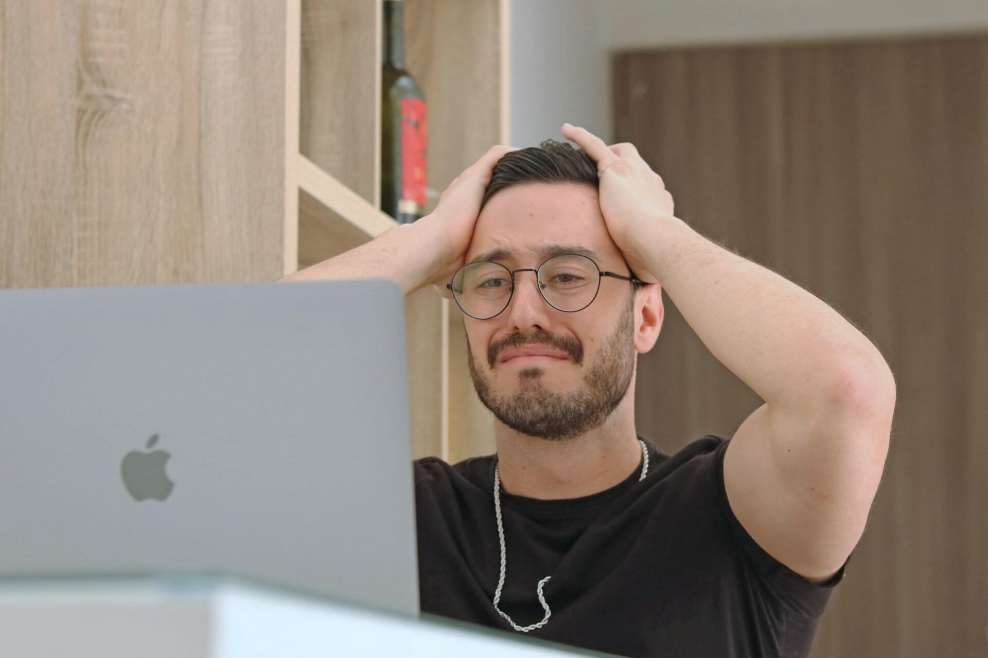 Man holding his head while looking at a laptop