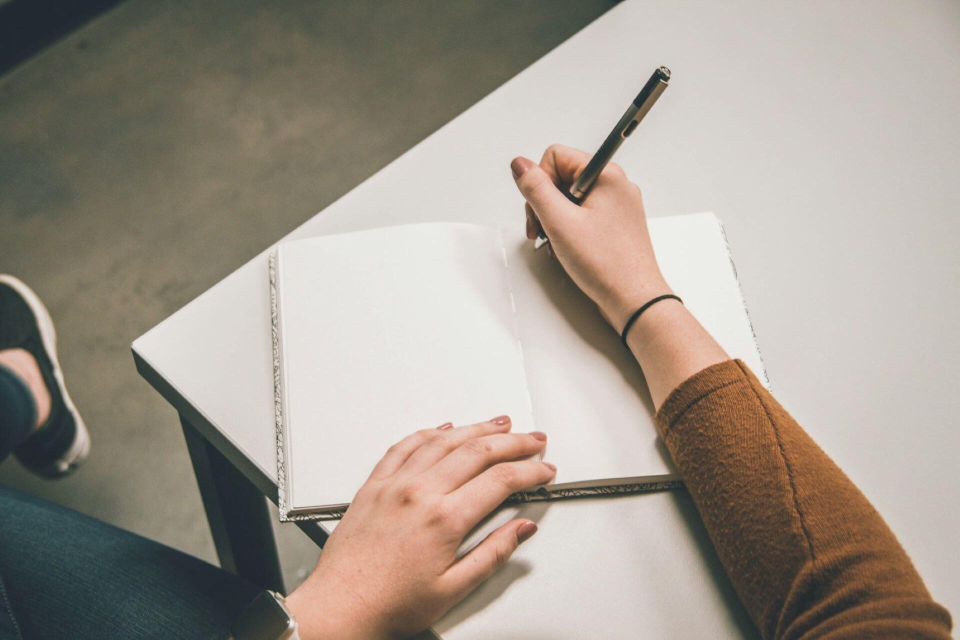 Person writing in a blank notebook at a table
