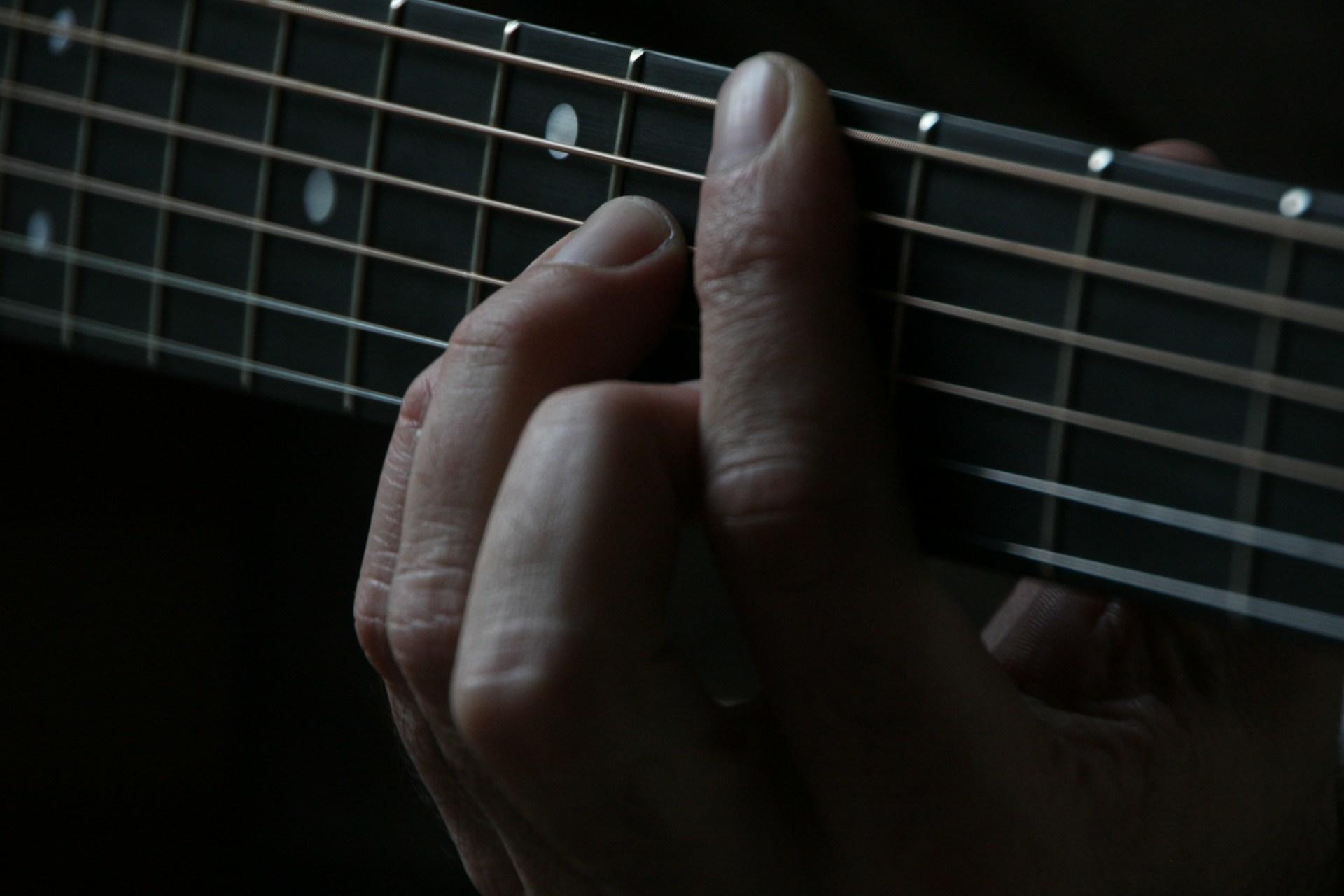A closeup of a person fretting a barre chord on a guitar.