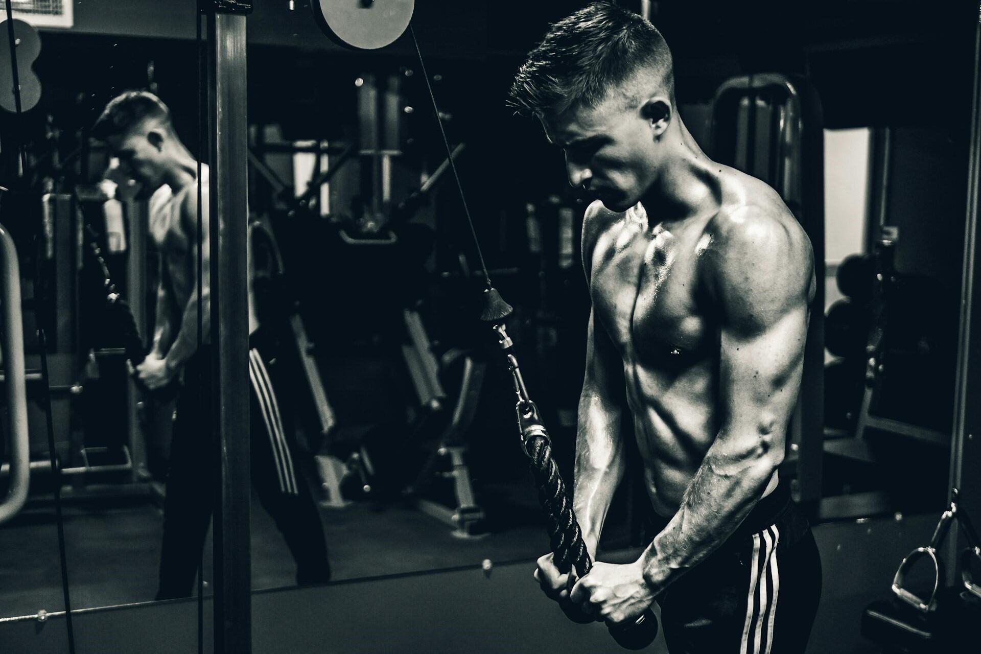 Person using a cable machine for a triceps exercise in a gym with mirrors and weight machines
