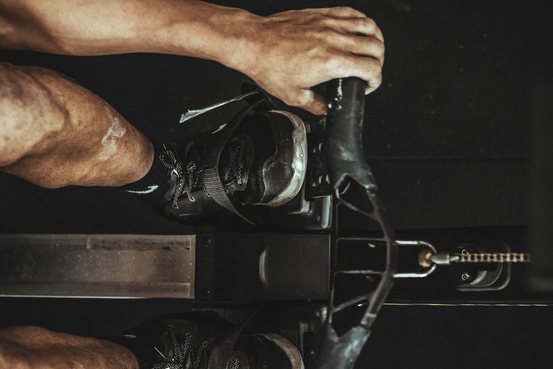 Close-up of a person’s hands and feet using a rowing machine in a gym