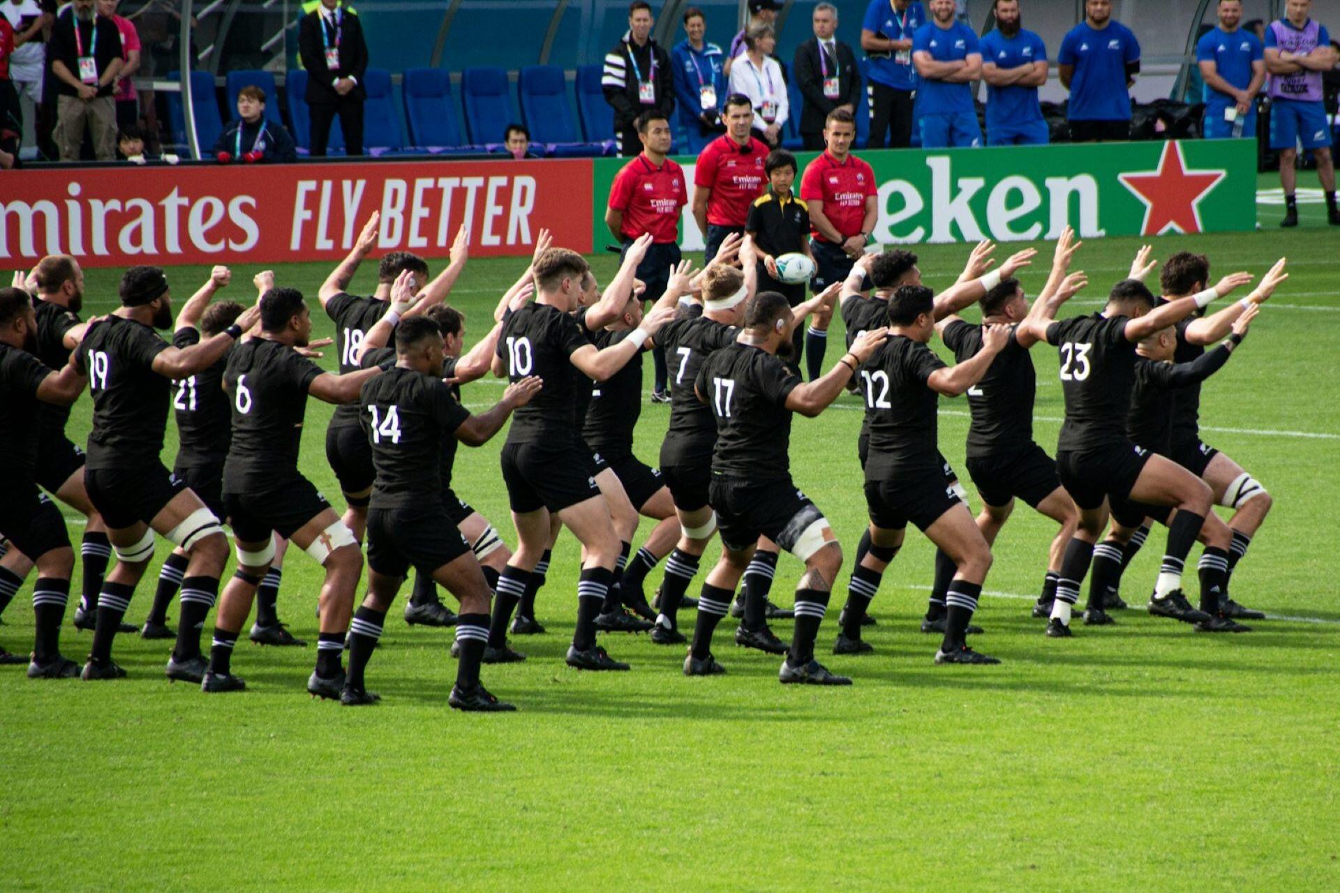 Rugby players in black uniforms performing a haka on a grass field