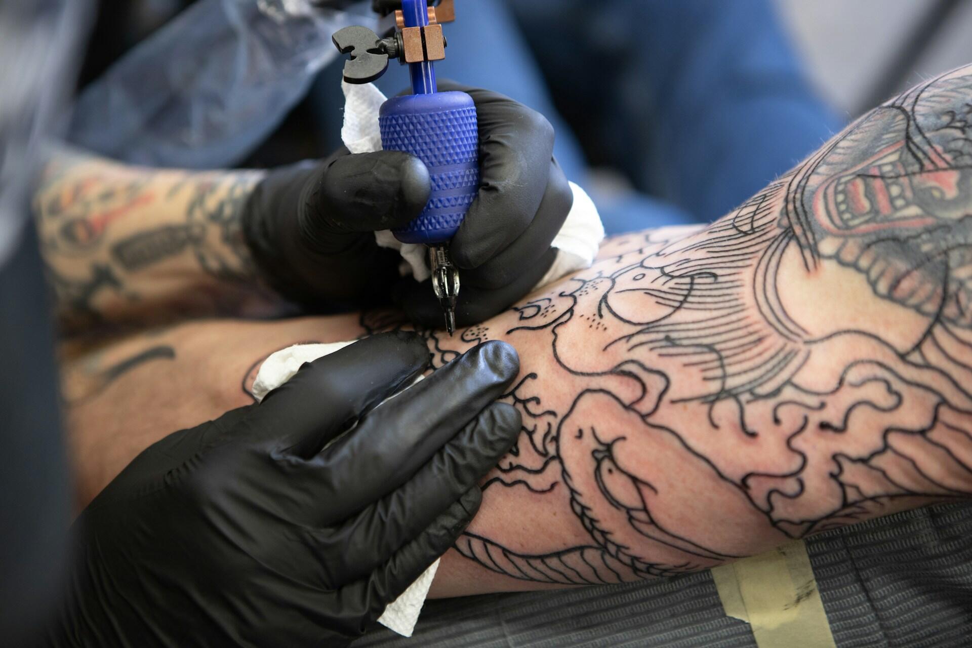Tattoo artist wearing black gloves tattooing a patterned design on an arm