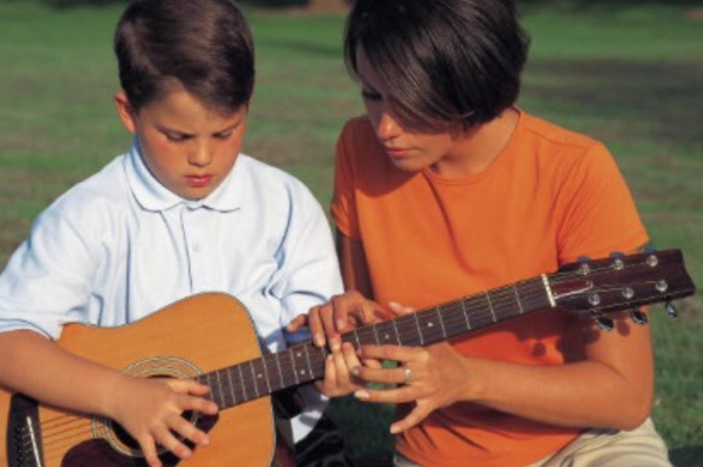 A woman teaches a boy how to play guitar.