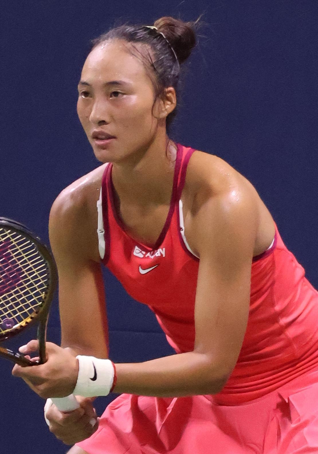 A woman in a red tank top holding a tennis racket