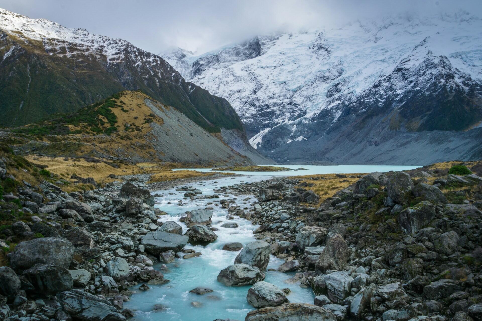 Glacial river flowing into Hooker Lake beneath snow-covered mountains in Aotearoa.
