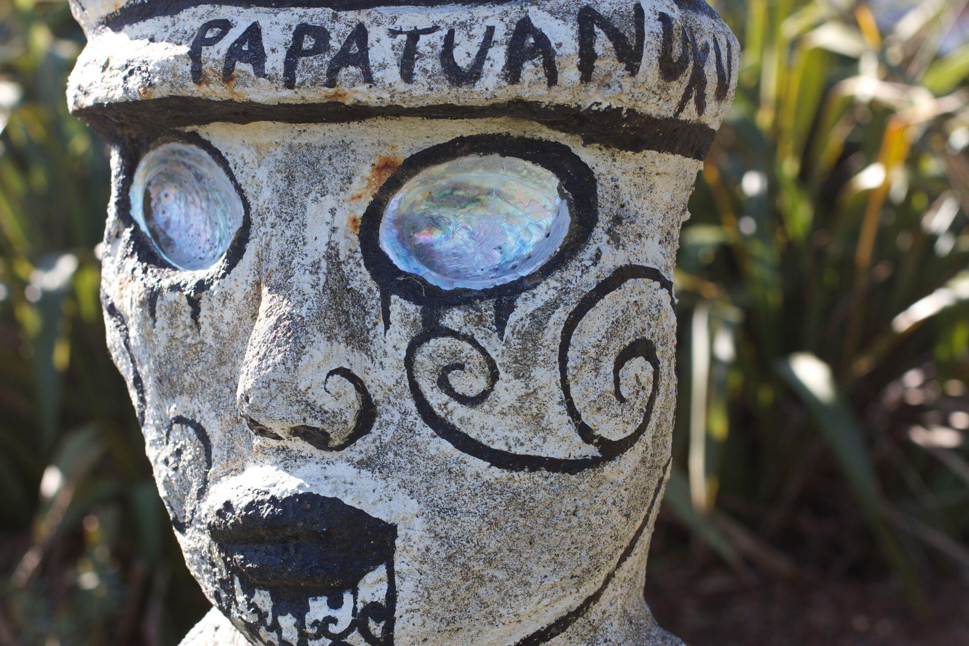 Sculpted figure representing Papatūānuku with stylised facial markings and shell inlay eyes.