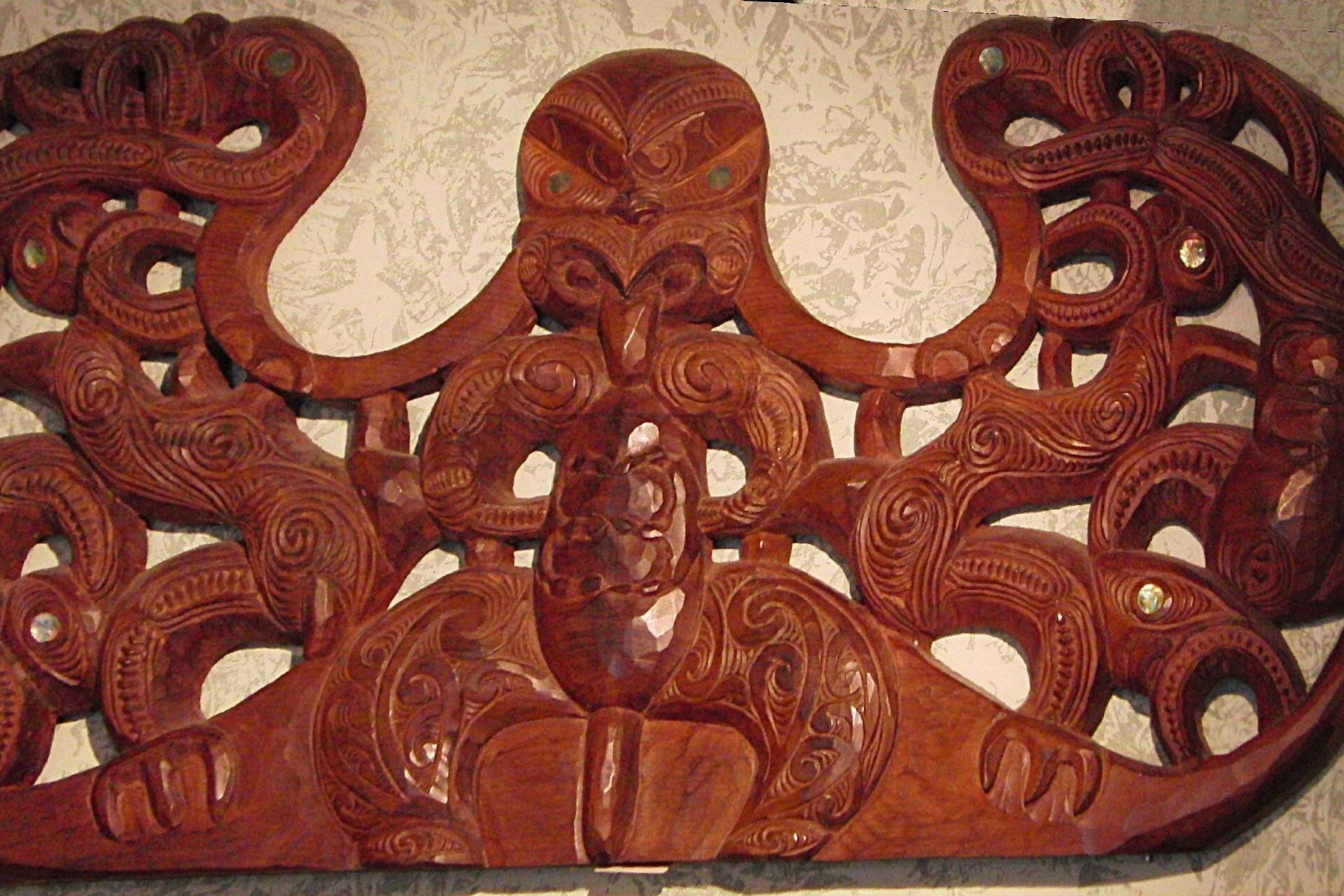 Carved wooden manaia figure with intricate spirals and openwork patterns in traditional Māori style.