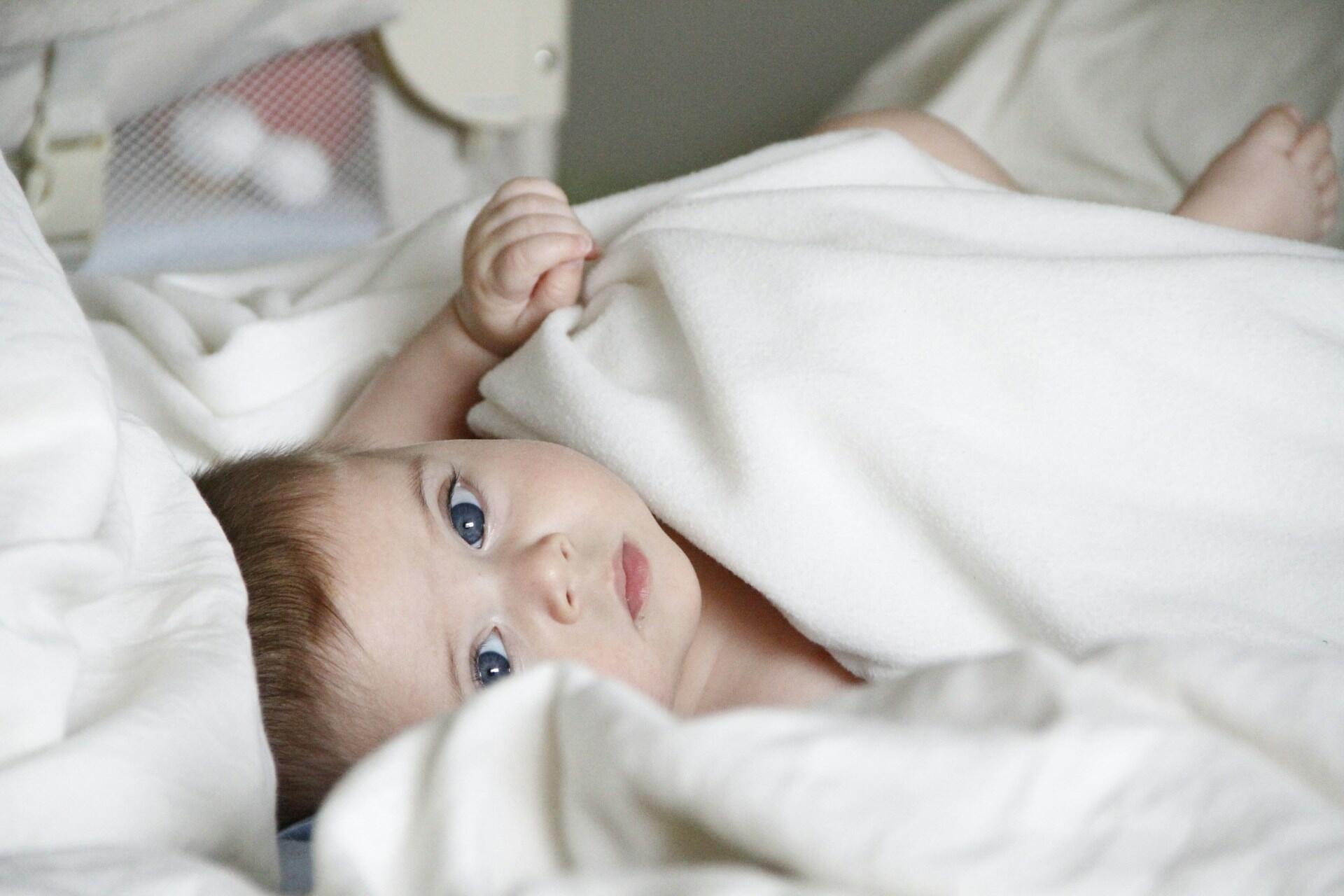 baby lying under white blanket looking at camera