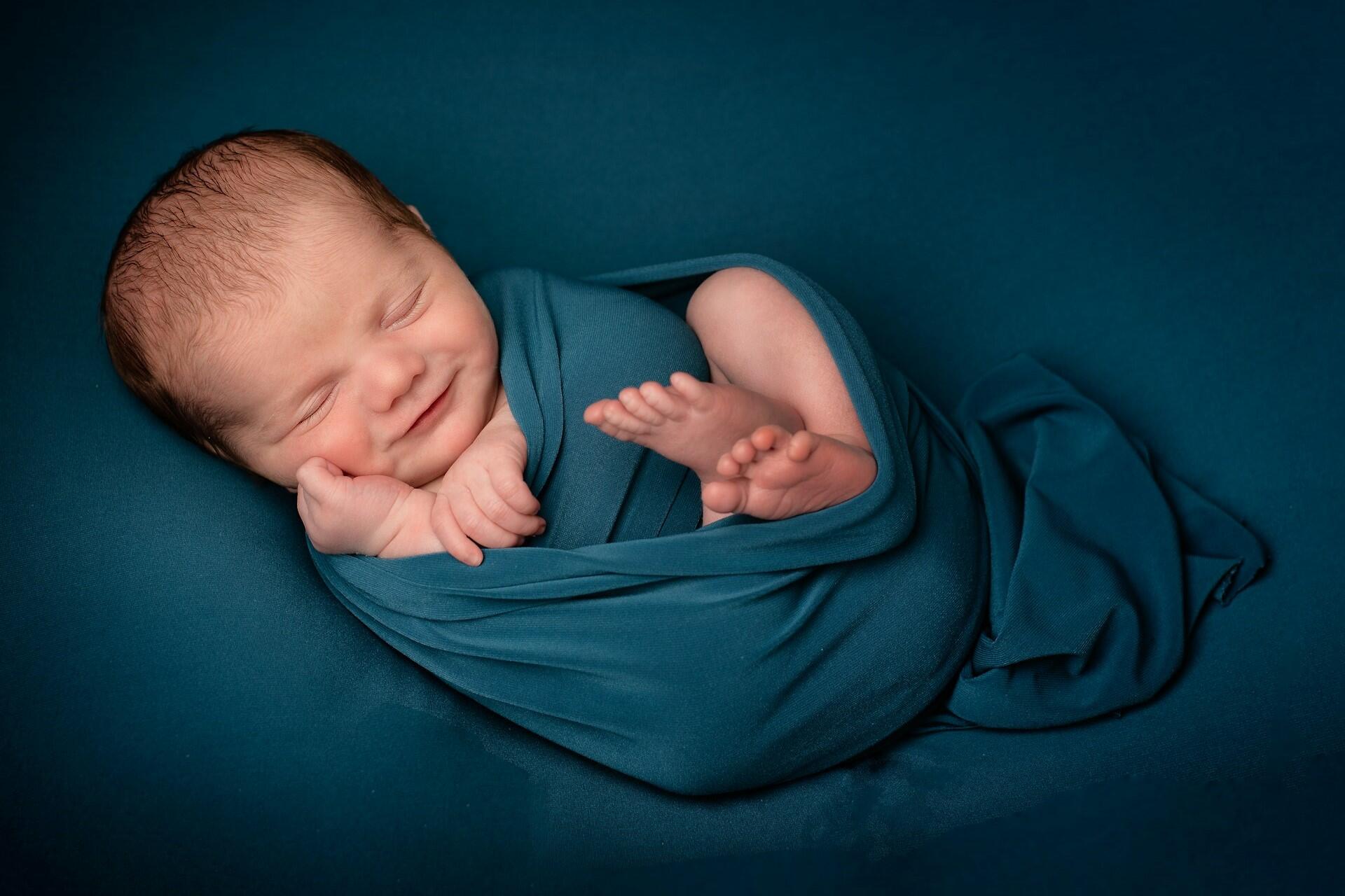 Sleeping baby wrapped in blue cloth on dark background