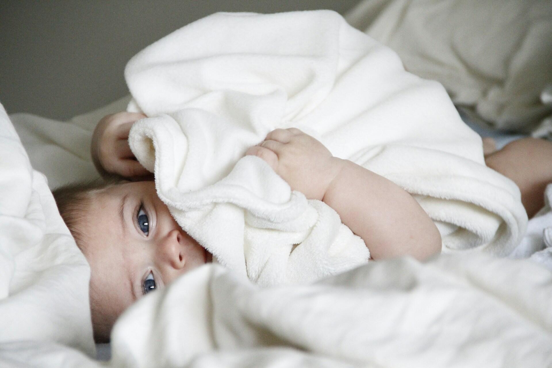 baby holding white blanket covering face