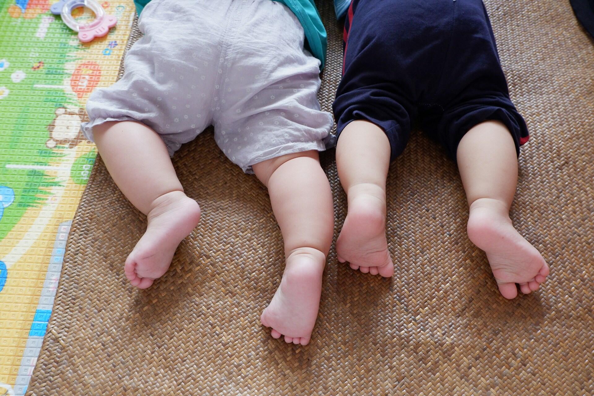 Two babies legs lying side by side on mat