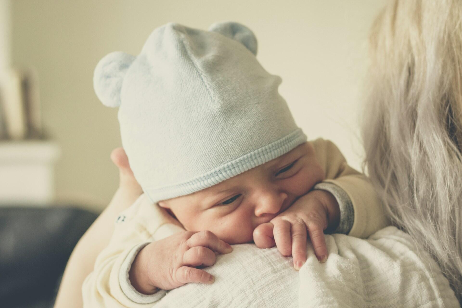 Baby wearing hat resting on adult shoulder