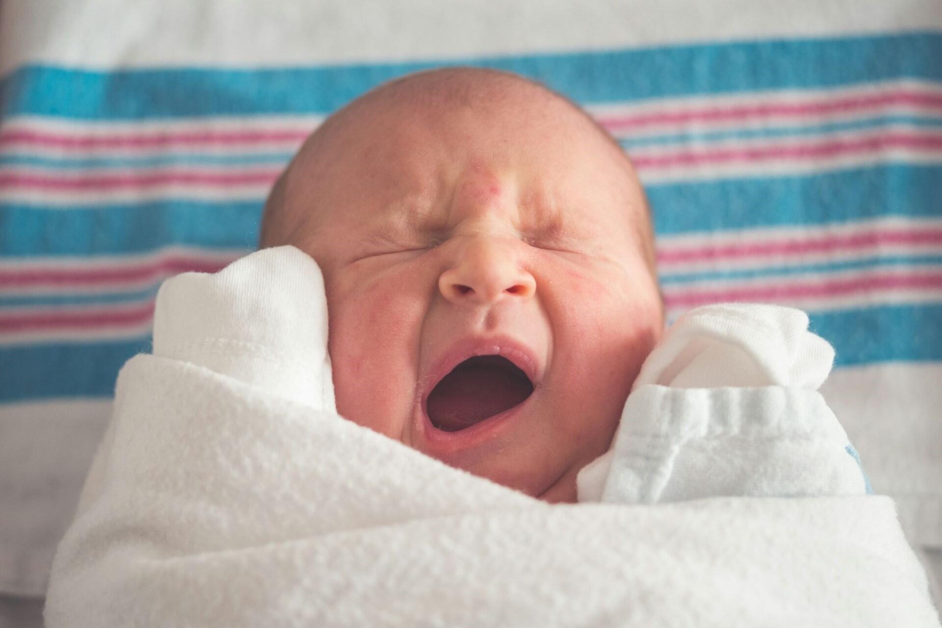 newborn baby yawning wrapped in hospital blanket