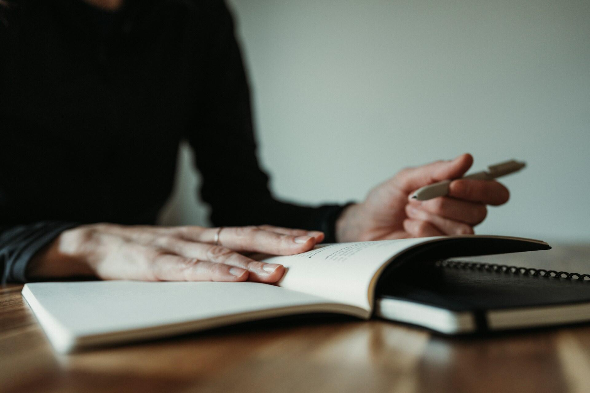open book with hand holding a pen while studying