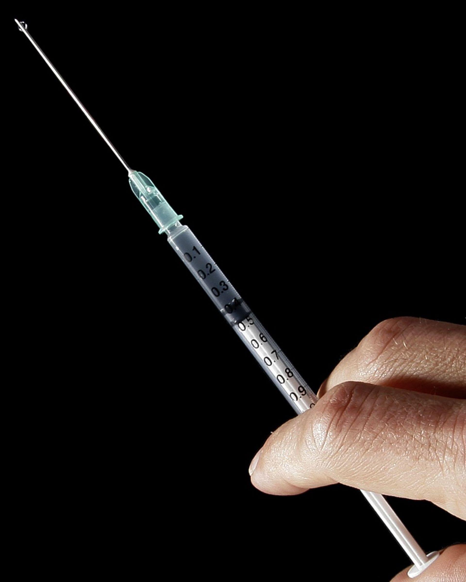 Hand holding a clear plastic disposable syringe against a black background