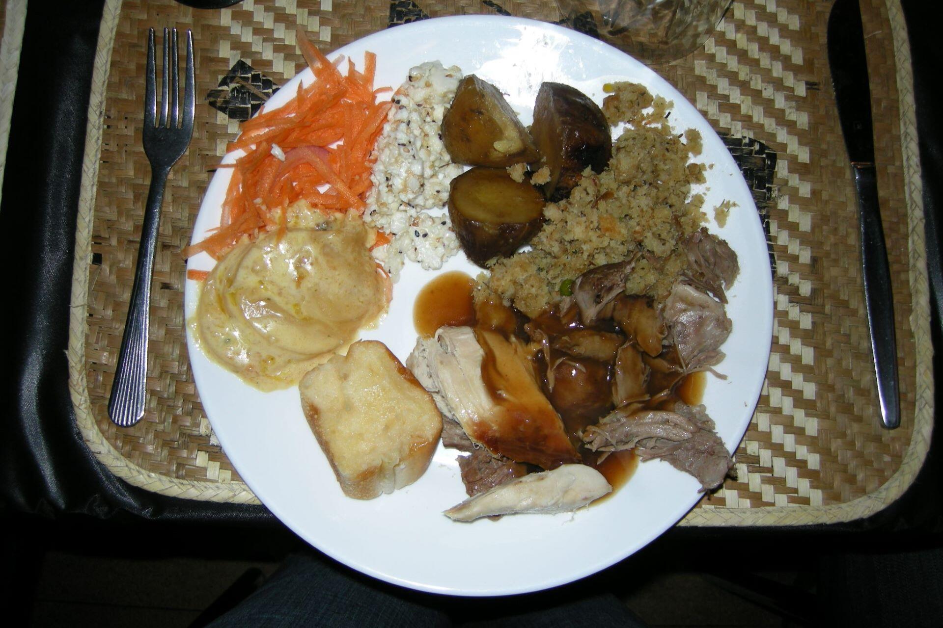 Plate of hāngī meal with meat, potatoes, vegetables, and sides on a woven tray
