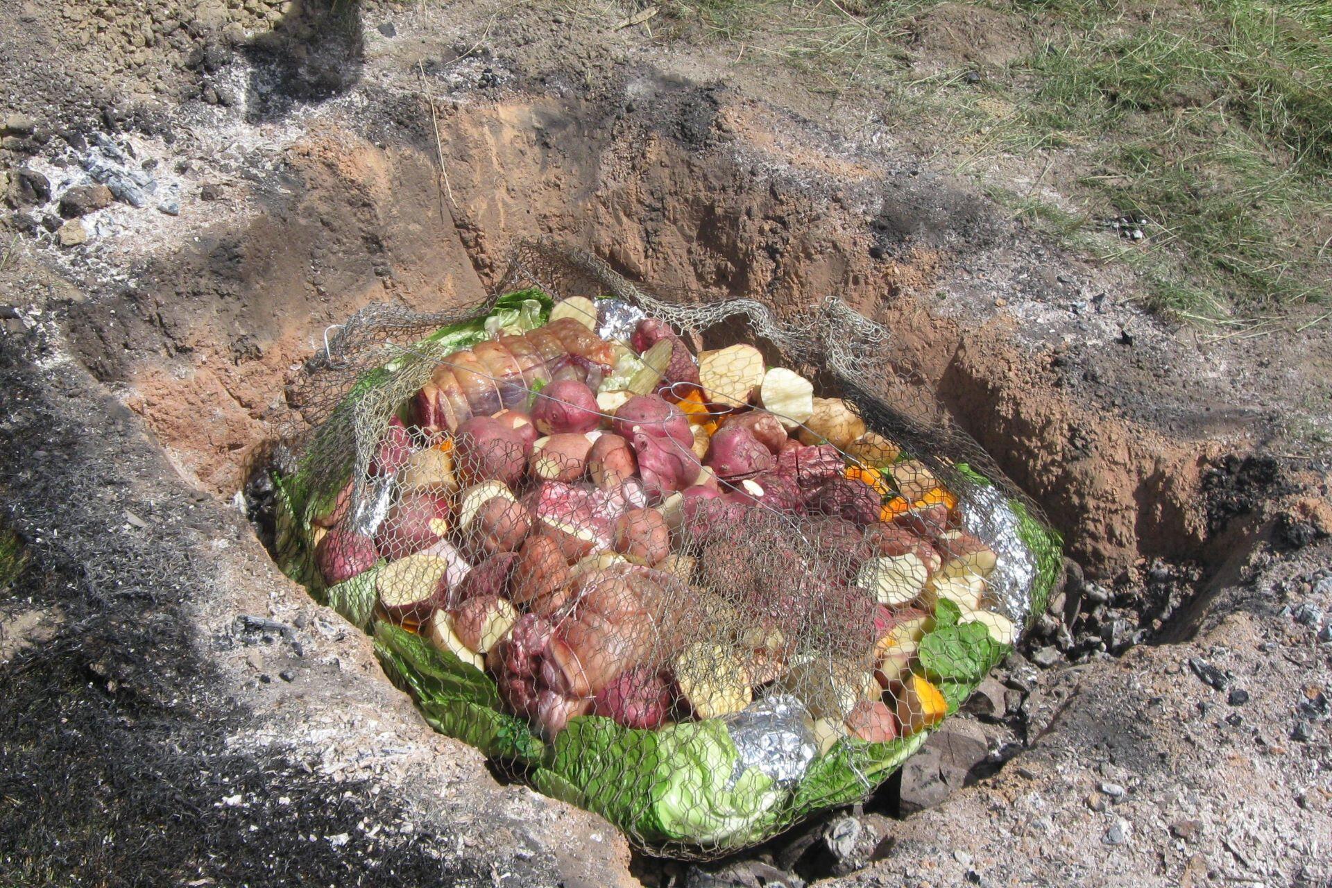 Food wrapped and placed in a traditional hāngī pit with hot stones and soil surrounding it