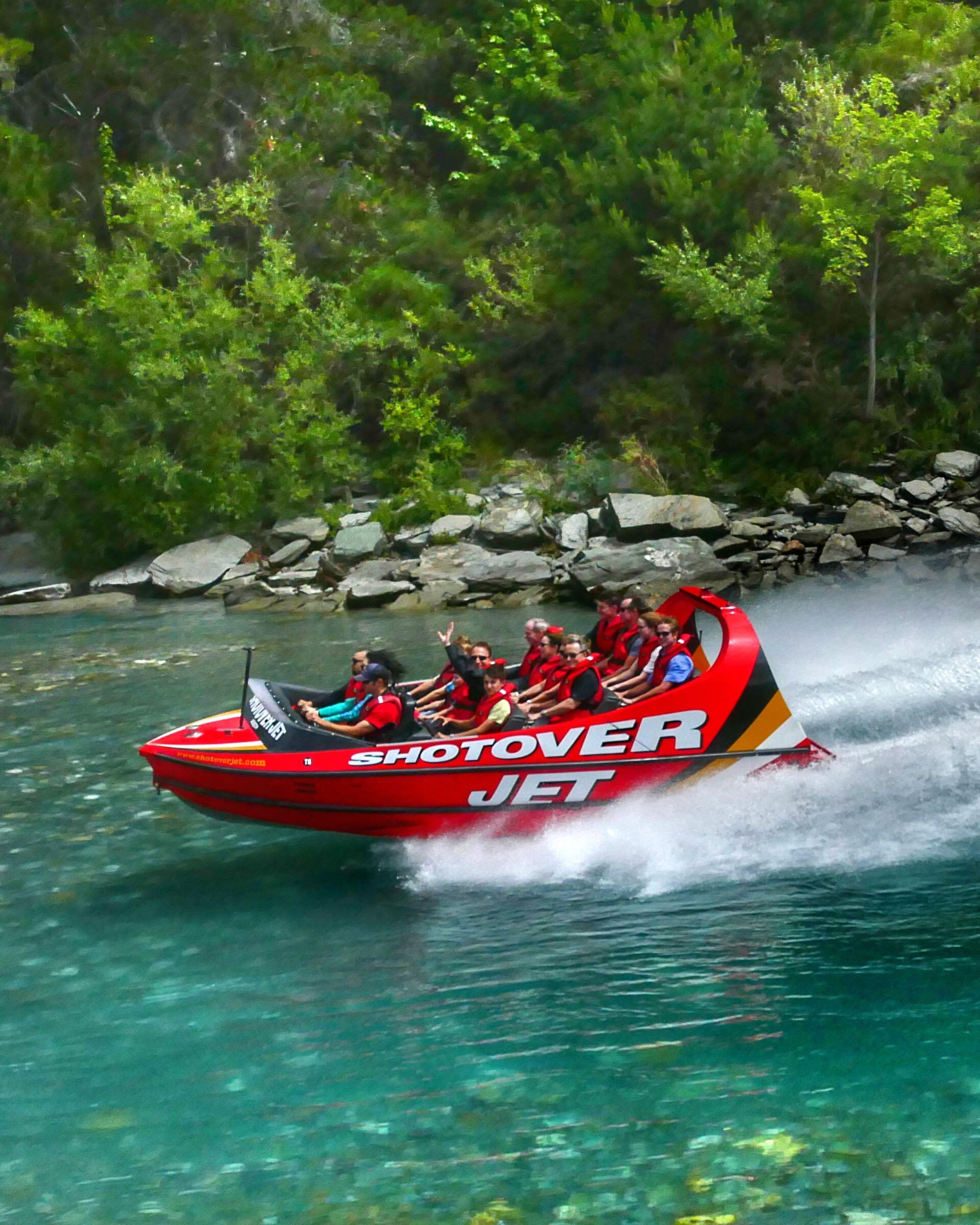 Red jet boat carrying passengers at high speed on a river with water spray