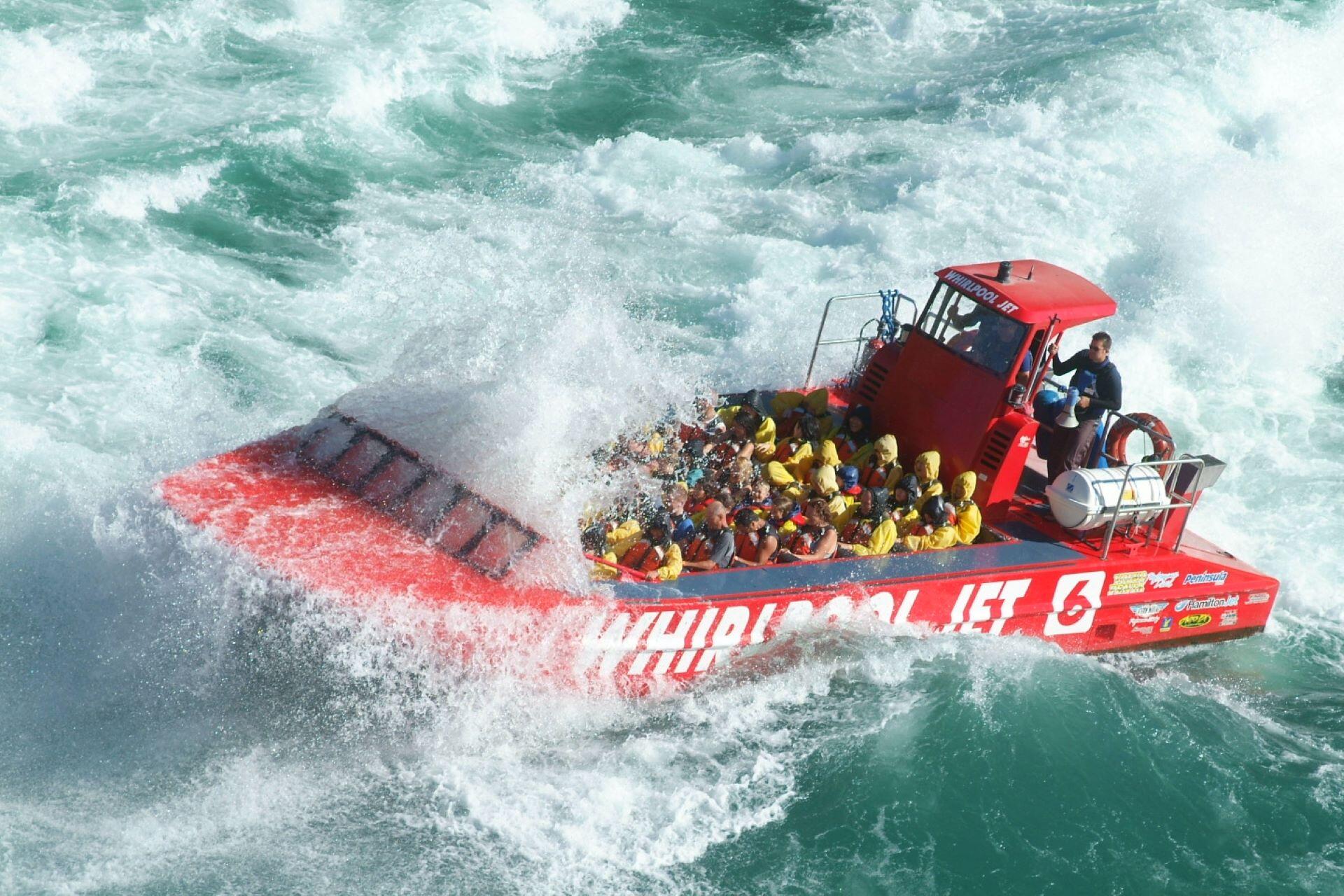 Red jet boat navigating rough water with passengers wearing safety gear