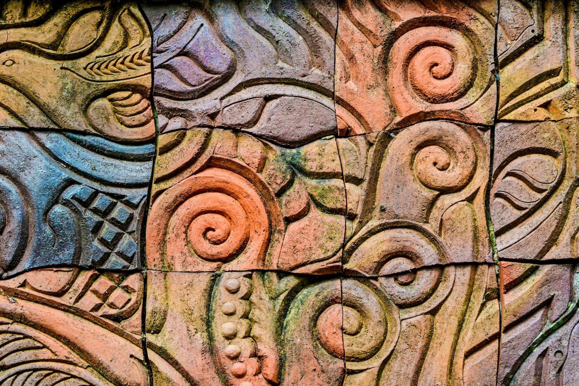 detailed Māori carving patterns with spirals and figures on a textured wall