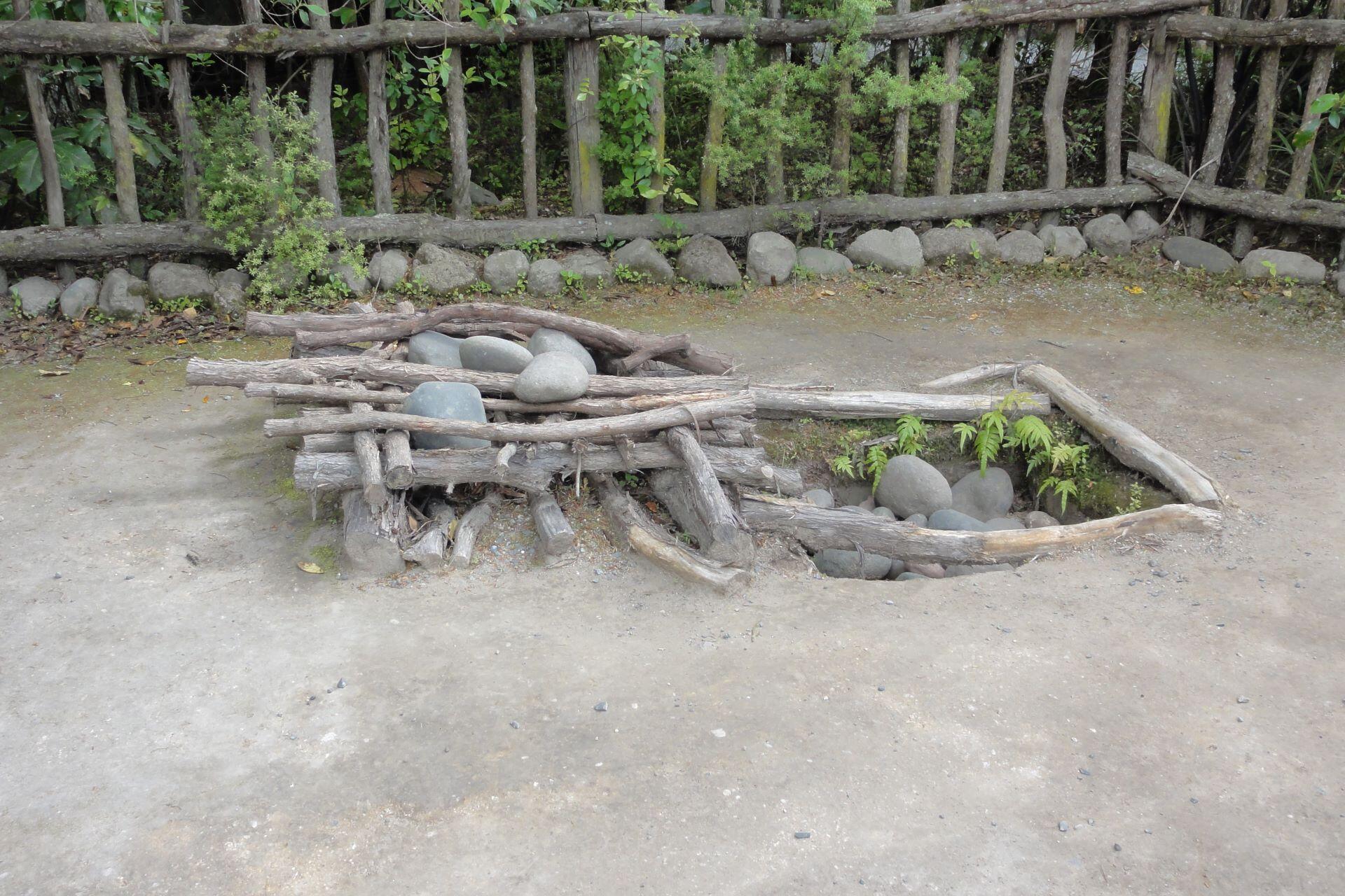 Wooden structure with logs and stones arranged for heating in a traditional cooking setup