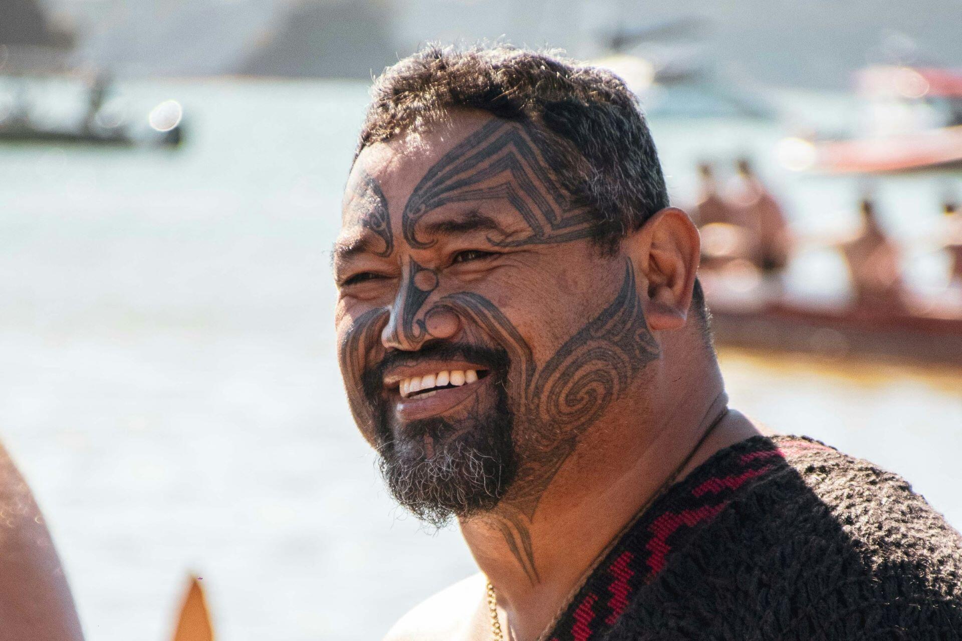 man with traditional Māori facial tattoo smiling outdoors