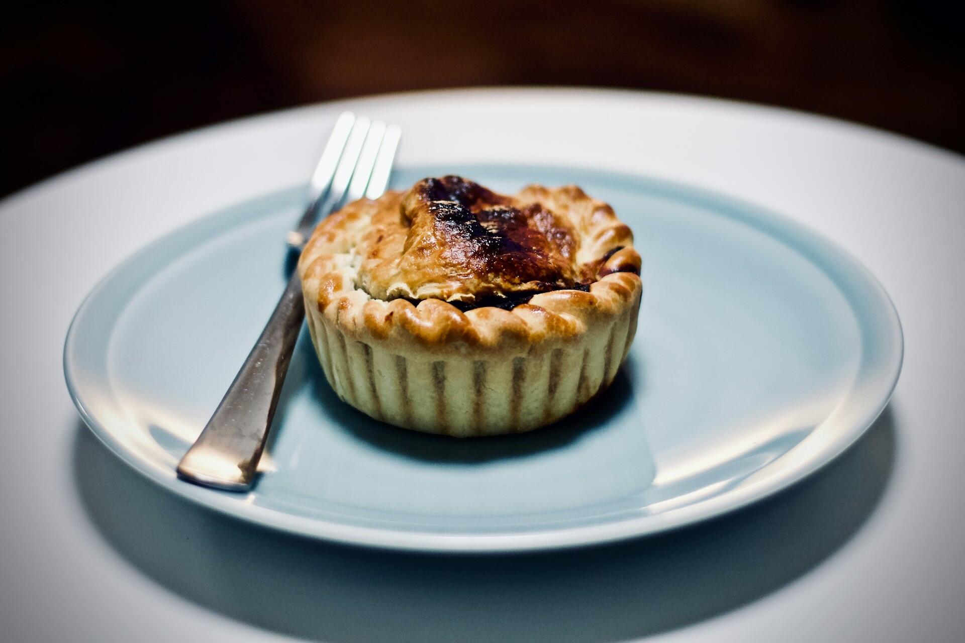 Individual meat pie with golden crust on a plate with a fork beside it