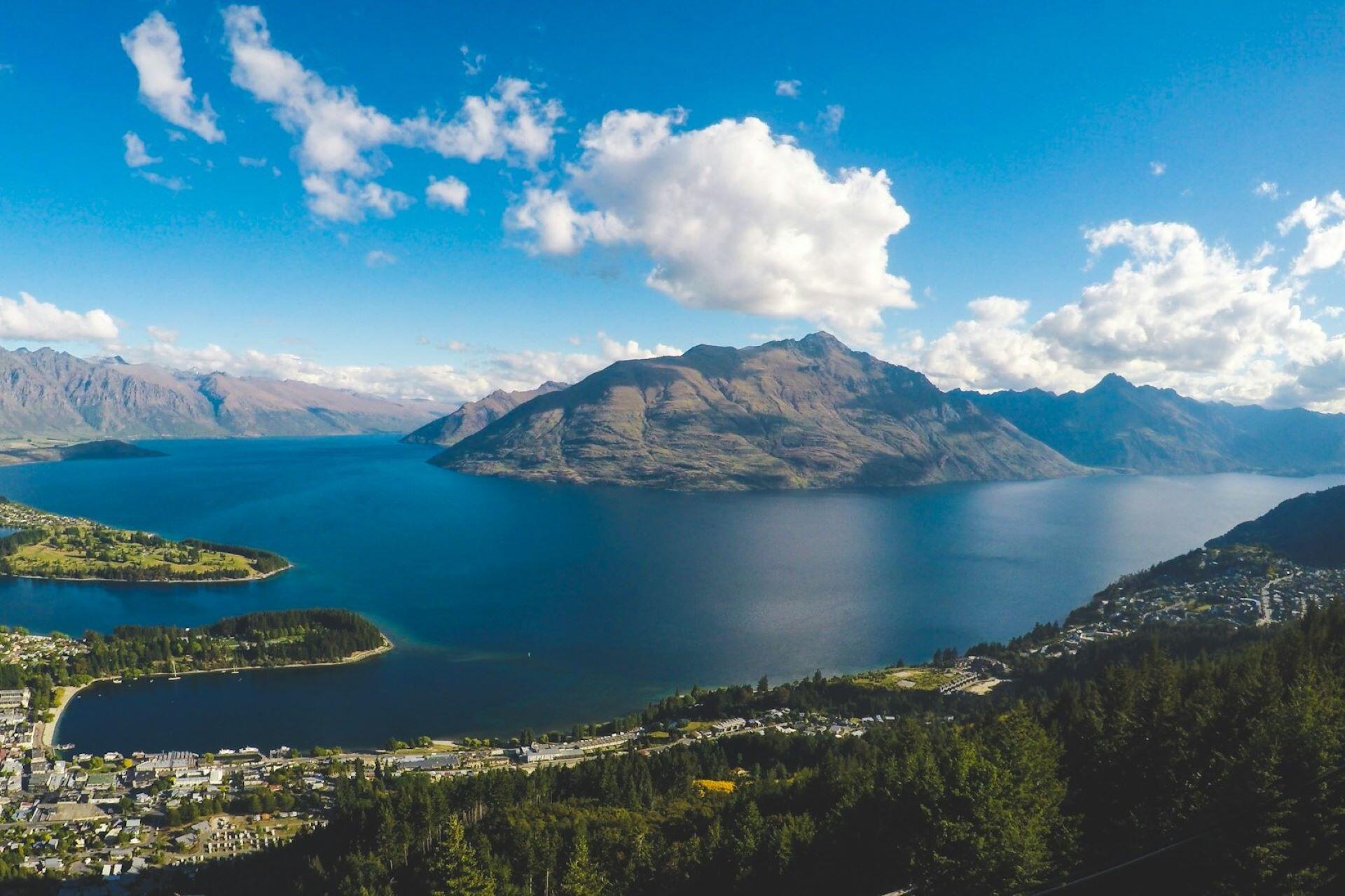 lake surrounded by mountains with a town in the foreground under a blue sky