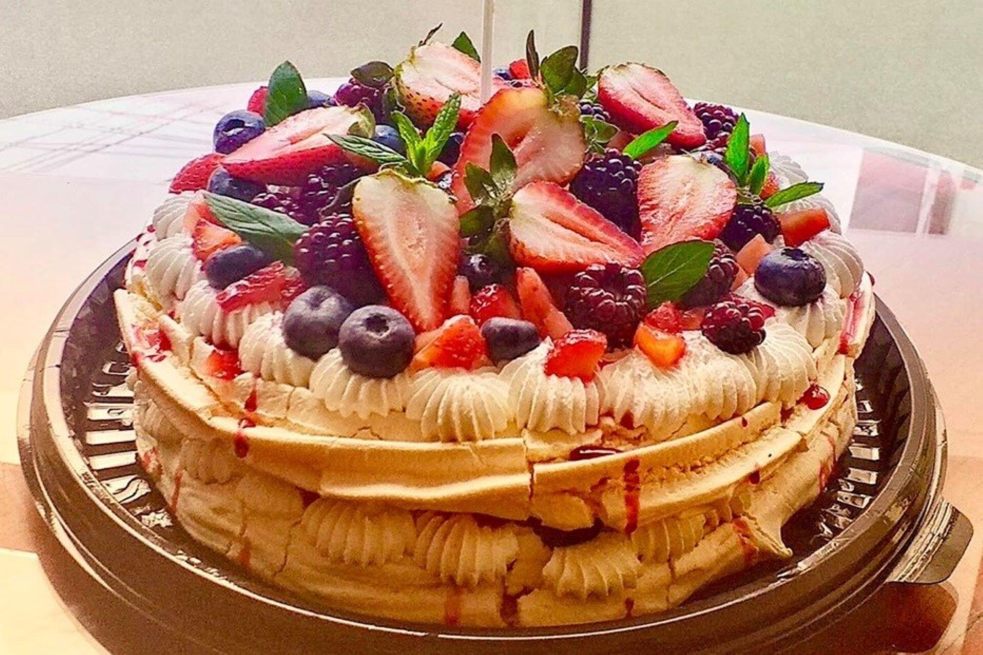 pavlova topped with strawberries blueberries raspberries and whipped cream on serving tray