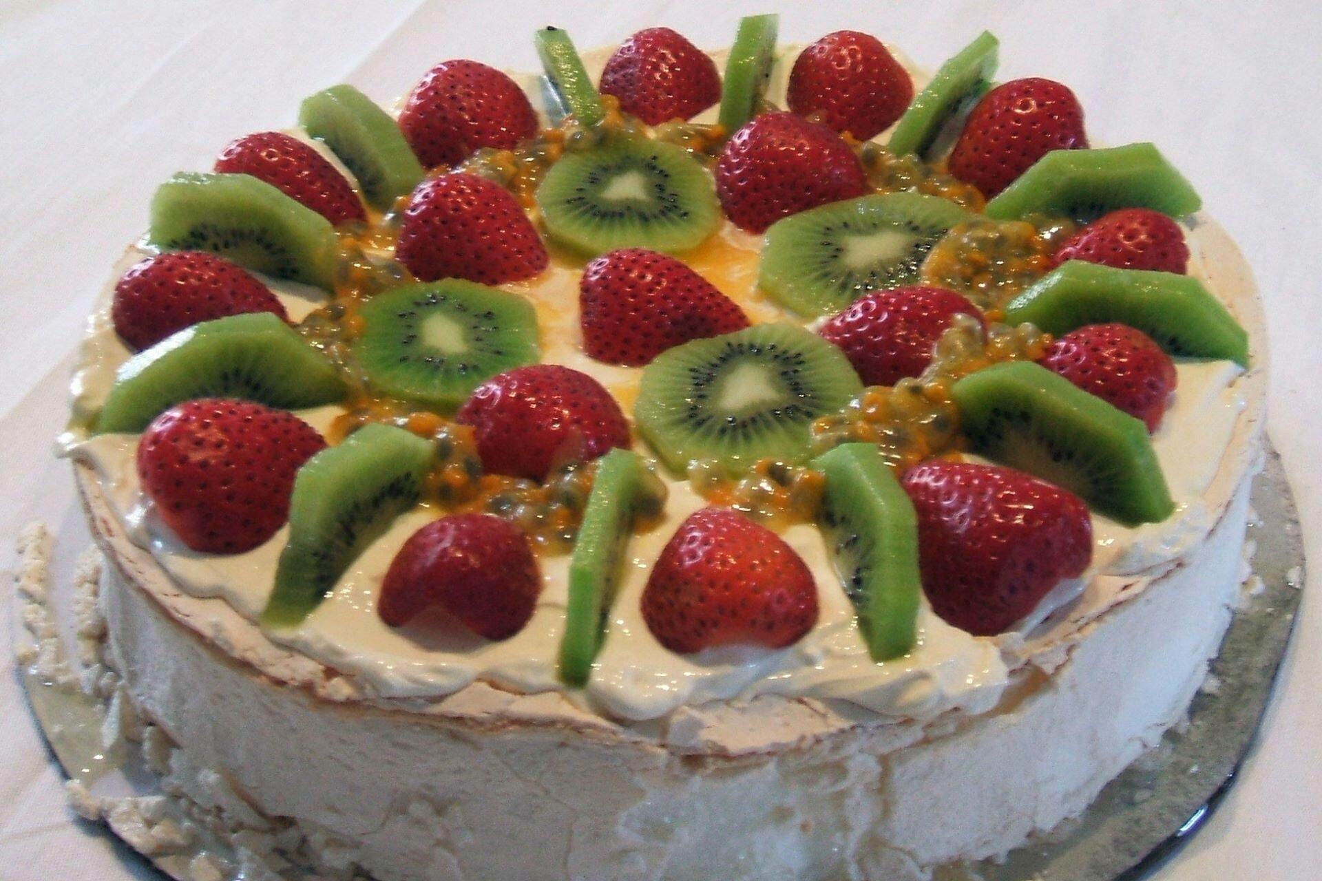 Pavlova topped with sliced kiwi fruit, strawberries, and passionfruit on a cream base