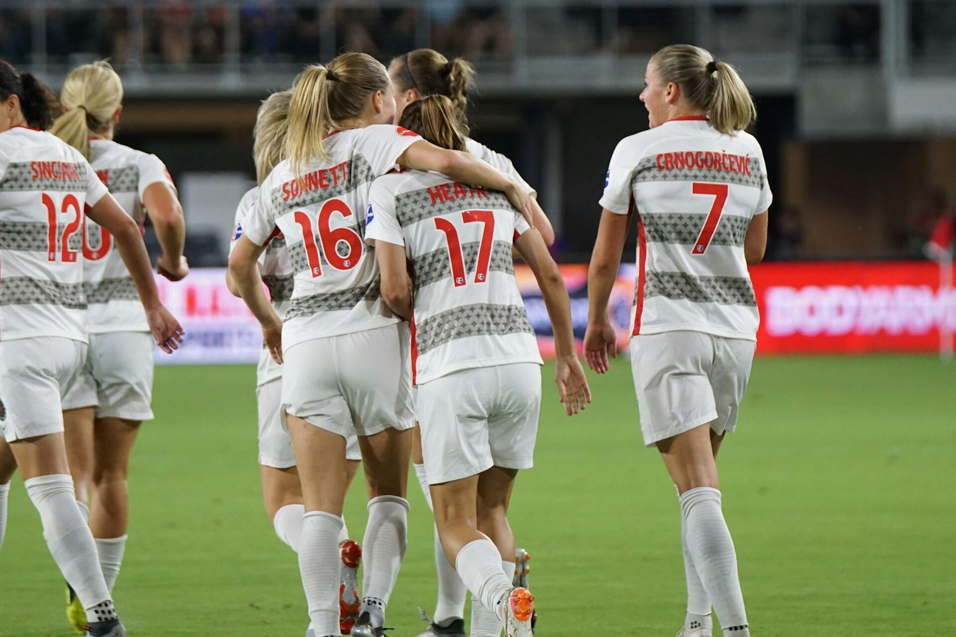 Women football players in white kits walking on the pitch